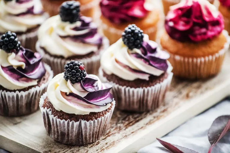 Mehrere frisch gebackene Schoko-Muffins, verziert mit einer lila-weißen Creme und einer Brombeere