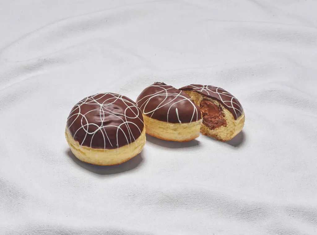 Zwei Nougat-Krapfen aus der INTERSPAR-Backstube legen auf einem weißen Tuch wobei einer der Krapfen mittig halbiert ist
