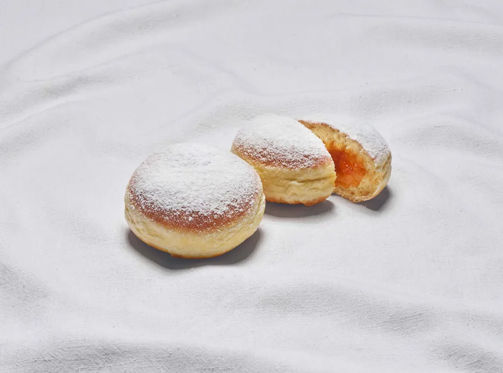 Zwei Marillen-Krapfen aus der INTERSPAR-Backstube legen auf einem weißen Tuch wobei einer der Krapfen mittig halbiert ist