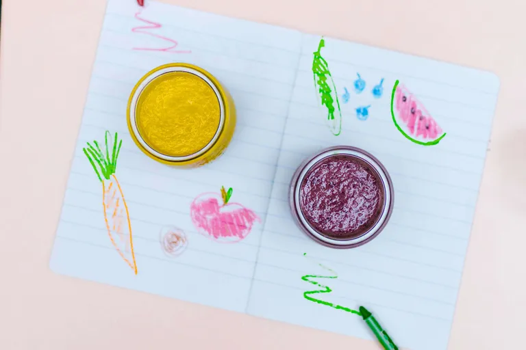 Zwei Gläser mit Frucht-Smoothies auf einer bemalten Unterlage als gesunder Snack für Kinder