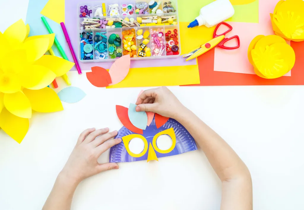 Child crafting a colorful paper mask with feathers and a variety of art supplies, including markers, glue, and decorative items.