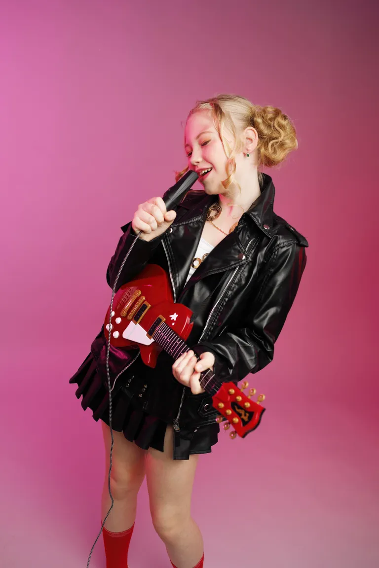 Ein Mädchen verkleidet als Rockstar mit Lederjacke und Spielzeuggitarre