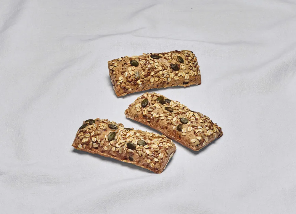 Drei Kraftriegel mit Körnern, garniert mit Haferflocken, Kürbiskernen und Leinsamen, vor einem weißen Stoffhintergrund.