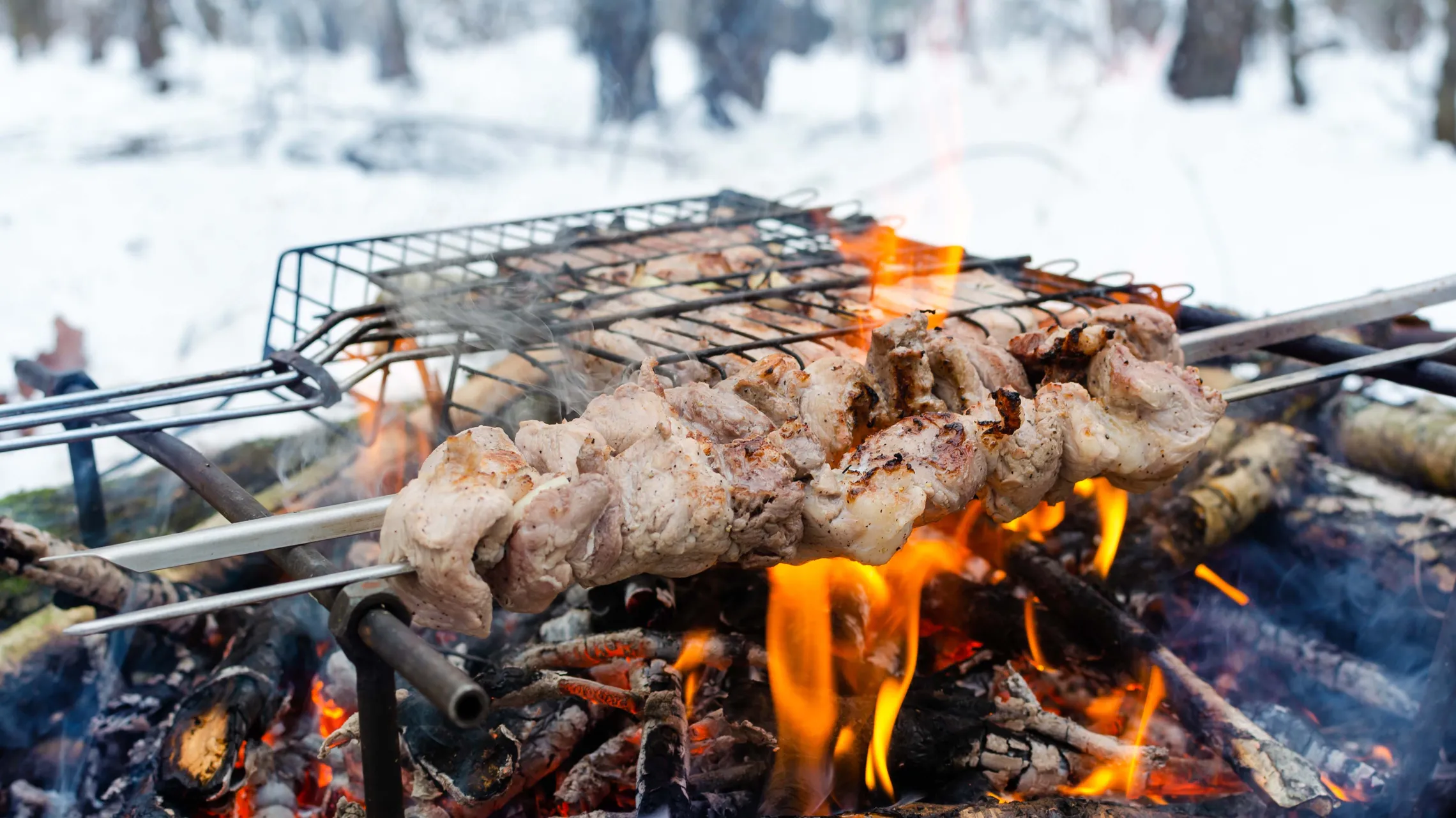 Fleischspieße und Grillrost über offenem Feuer beim Wintergrillen im Schnee