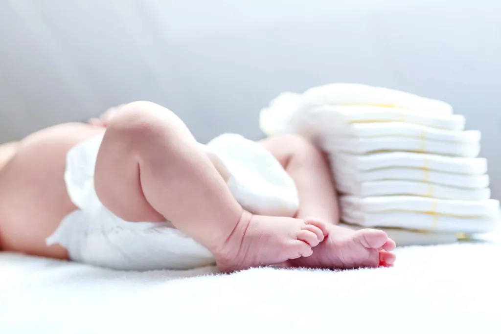 Baby liegt mit Windel neben einem Stapel frischer Windeln