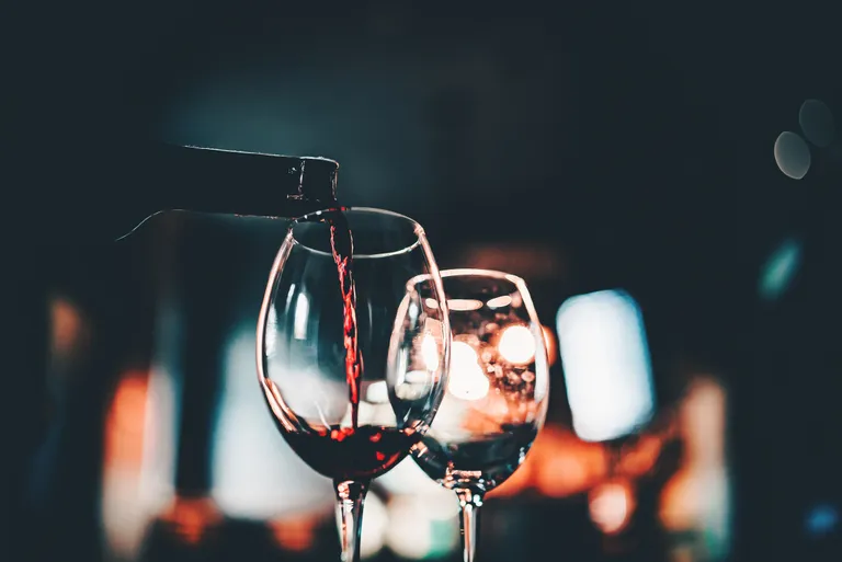 Rotwein wird in ein Glas gegossen, im Hintergrund ist alles verschwommen und es herrscht eine stimmungsvolle Beleuchtung.