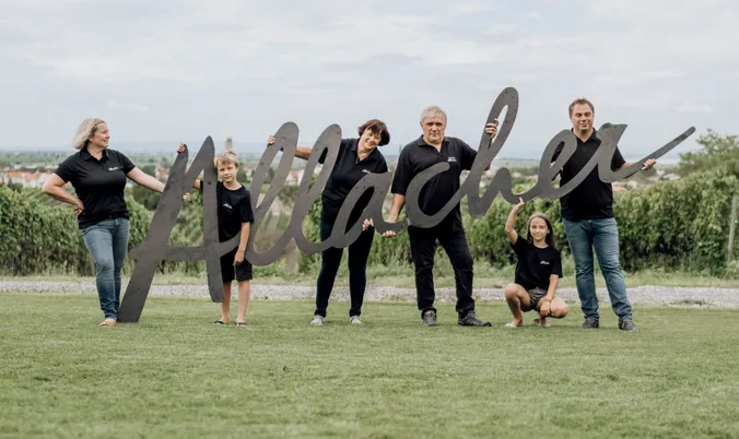 Sechs Personen in einheitlichen schwarzen T-Shirts stehen auf einer Wiese und halten ein großes Schild mit einer landschaftlichen Kulisse im Hintergrund in die Höhe.