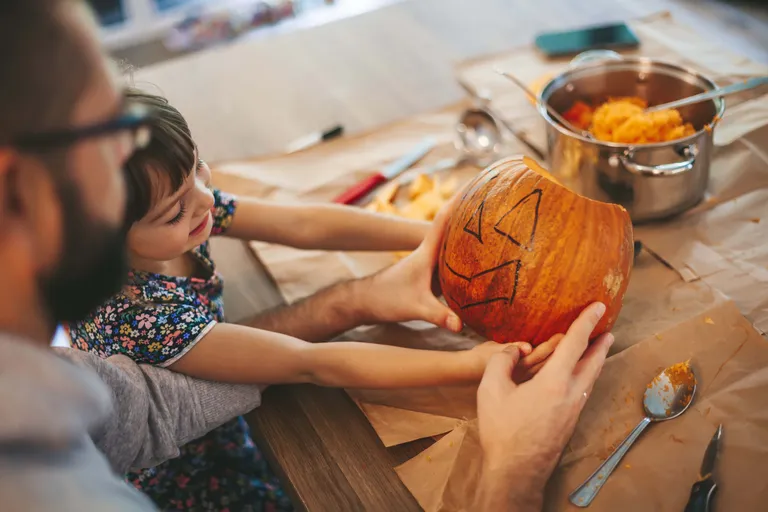 Ein Vater und ein kleines Mädchen beim gemeinsamen Schnitzen und Aushöhlen eines Kürbis für Halloween