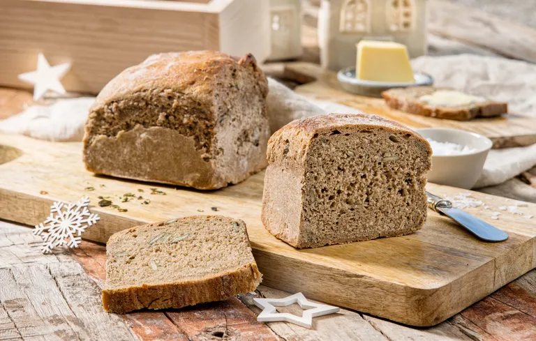 Geschnittenes Roggenbrot auf einem Holzschneidebrett mit Butter, einem Messer und einer weißen Schneeflockenverzierung auf einem rustikalen Tisch.