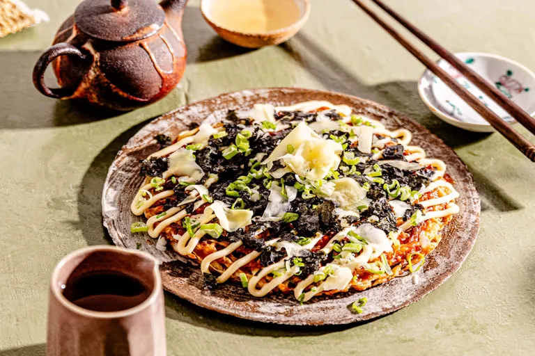 Japanisches Okonomiyaki mit Nori, Frühlingszwiebeln und Mayonnaise, serviert mit Tee und Essstäbchen