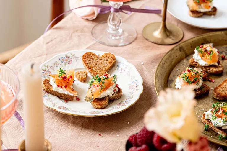 Kleine Brothappen mit Lachs und Frischkäse sowie herzförmiges Brot auf einem gedeckten Tisch