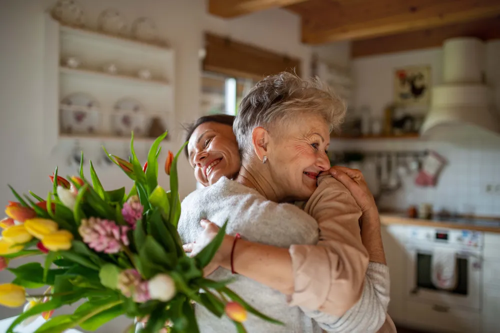 Eine erwachsene Tochter umarmt ihre Mutter und überreicht einen Blumenstrauß
