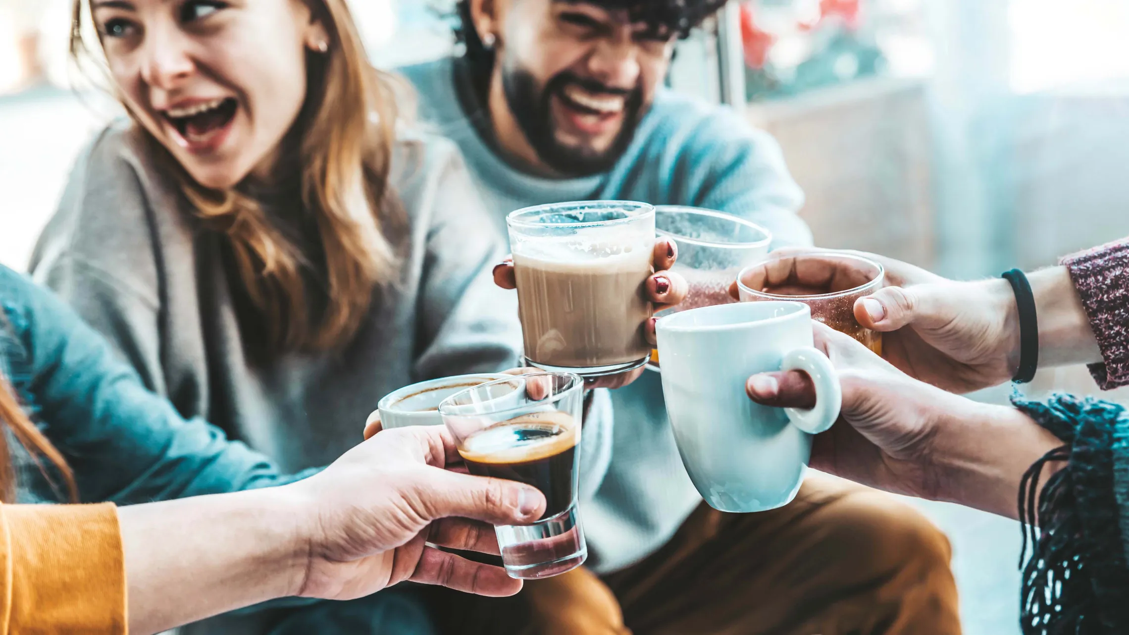Freundesgruppe stößt mit verschiedenen Kaffeegetränken und Heißgetränken an