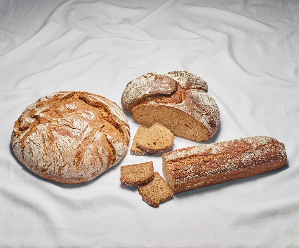 Drei verschiedene Großbrote der INTERSPAR-Bäckereien liegen mit aufgeschnittenen Scheiben Brot auf einem weißen Tuch