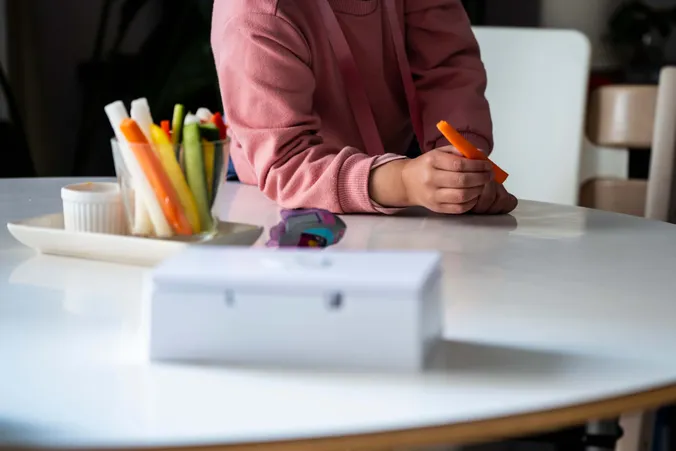 Kind hält eine Karottenstange neben einem Glas mit Gemüsesticks und Dip