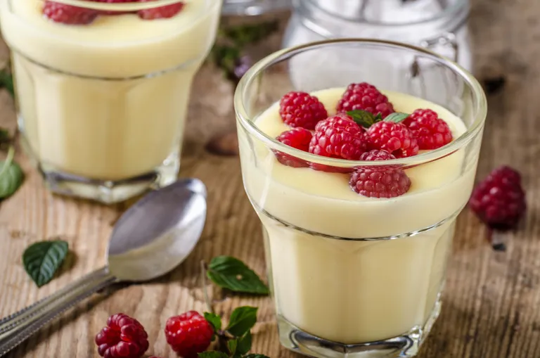 Cremiger Vanillepudding im Glas, garniert mit frischen Himbeeren und Minze