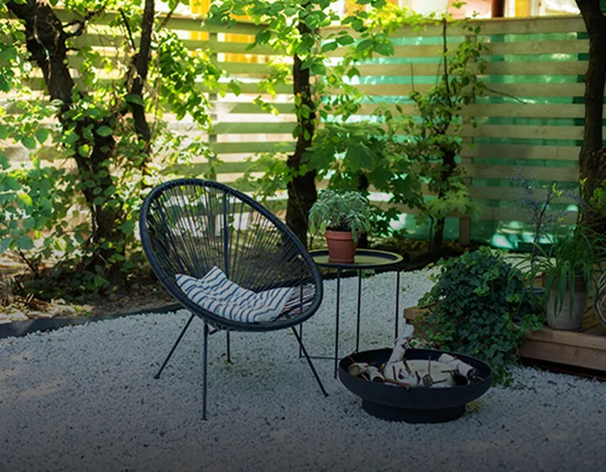 Ein schattiger Garten mit einem Loungesessel und einer Feuerschale, die nicht angezündet ist.