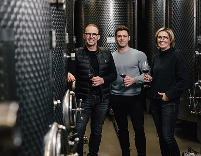 Drei Personen, die Weingläser in der Hand halten, stehen in einem Weingut, umgeben von großen Metallgärtanks.