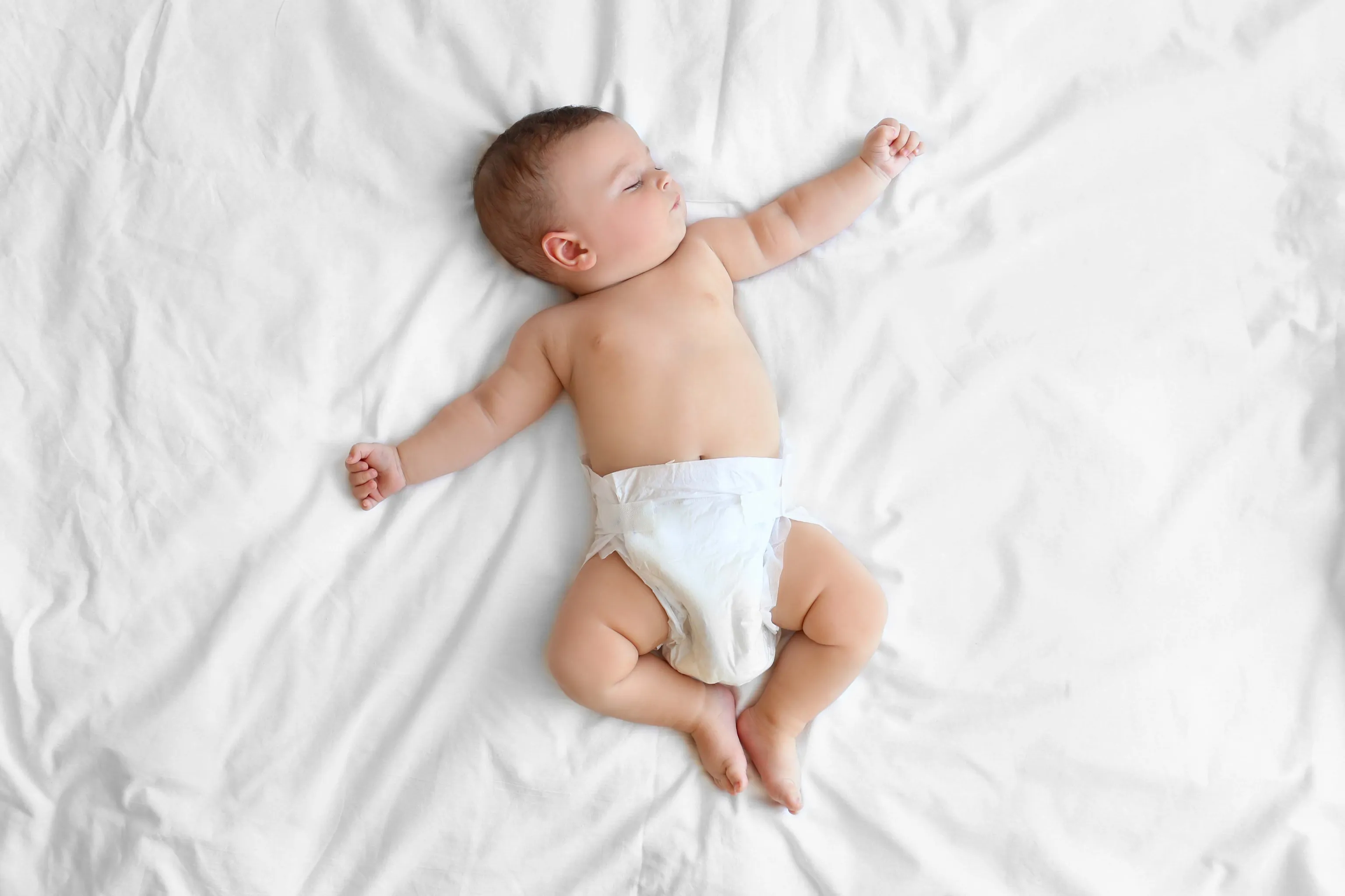 Baby liegt entspannt mit Windel auf einem weißen Bettlaken