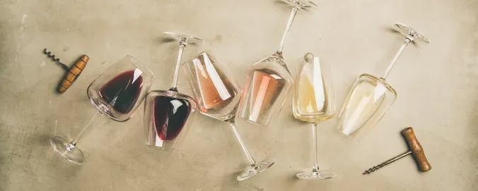 Sechs Weingläser mit verschiedenen Weinen, darunter Rot-, Rosé- und Weißwein, stehen auf einer strukturierten Oberfläche, auf der auch zwei Korkenzieher liegen.