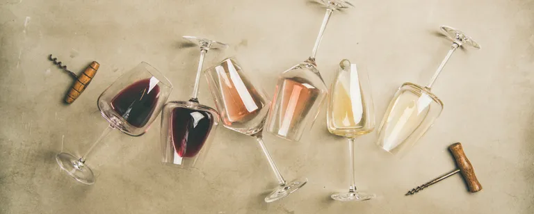 Sechs Weingläser mit verschiedenen Weinen, darunter Rot-, Rosé- und Weißwein, stehen auf einer strukturierten Oberfläche, auf der auch zwei Korkenzieher liegen.