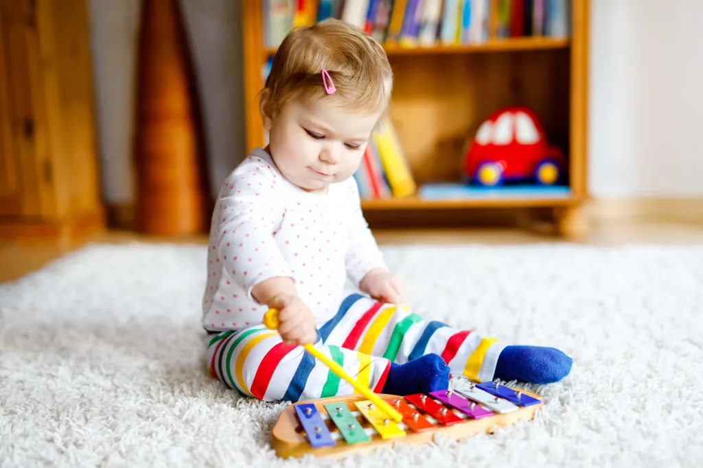 Kleinkind sitzt auf einem Teppich und spielt konzentriert auf einem bunten Xylophon