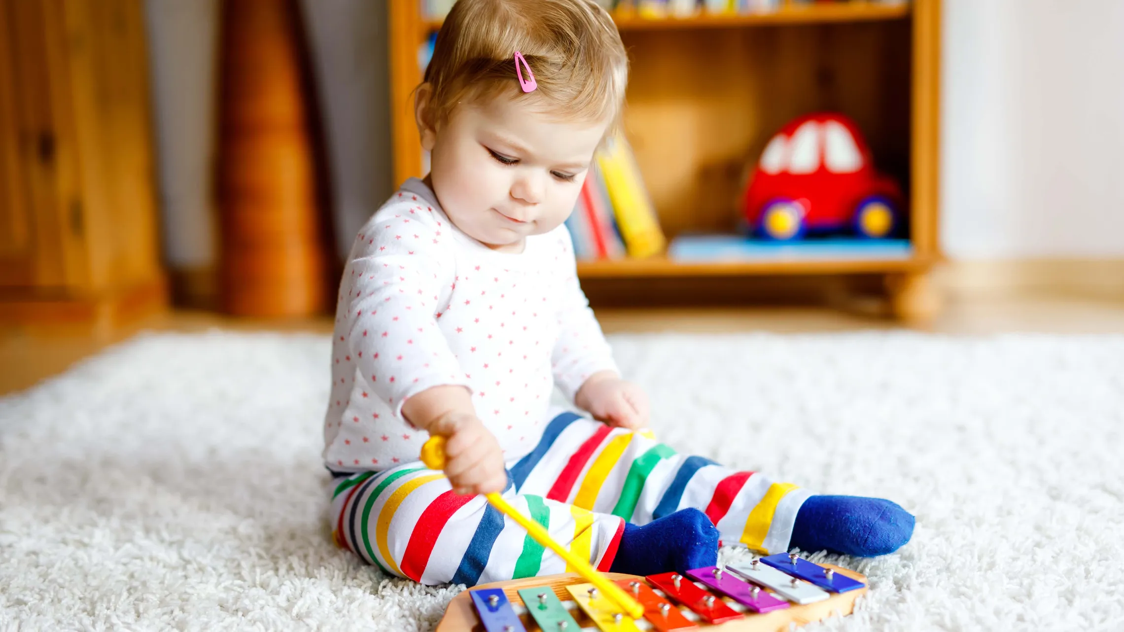 Kleinkind sitzt auf einem Teppich und spielt konzentriert auf einem bunten Xylophon