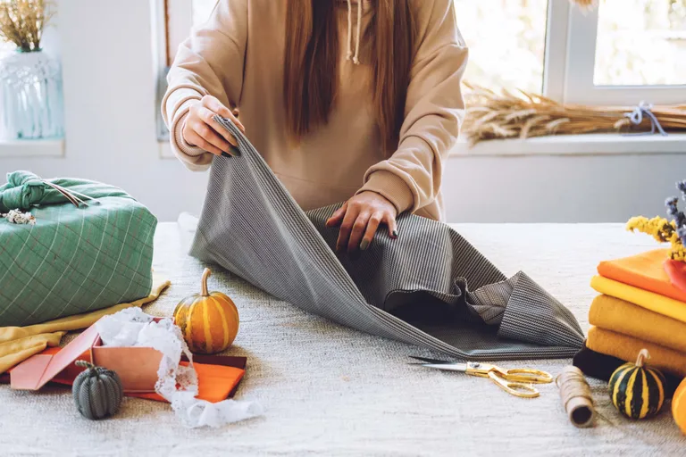 Eine Frau verpackt eine weiße Box mit einem Tuch im Stil japanischer Furoshiki