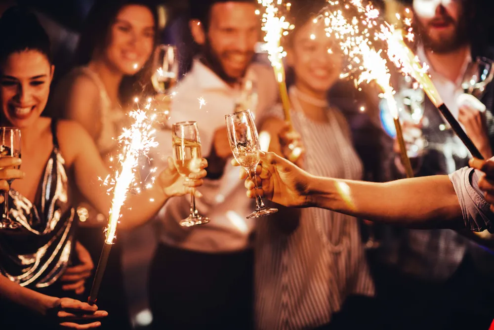 Group of people celebrating with sparklers and champagne glasses, smiling and toasting in a festive atmosphere.