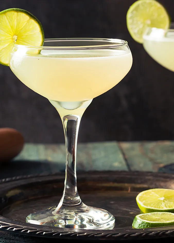 Klassischer Daiquiri im Coupette-Glas mit Limettenscheibe und frischen Limetten