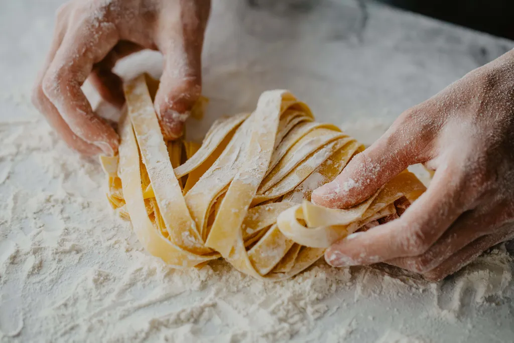 Hände formen frische Tagliatelle auf einer bemehlten Arbeitsfläche