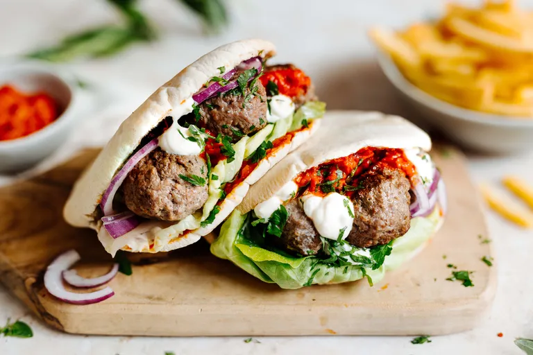 Gefüllte Cevapcici mit Fleischbällchen, Salat, roten Zwiebeln und Joghurtsauce auf Holzbrett