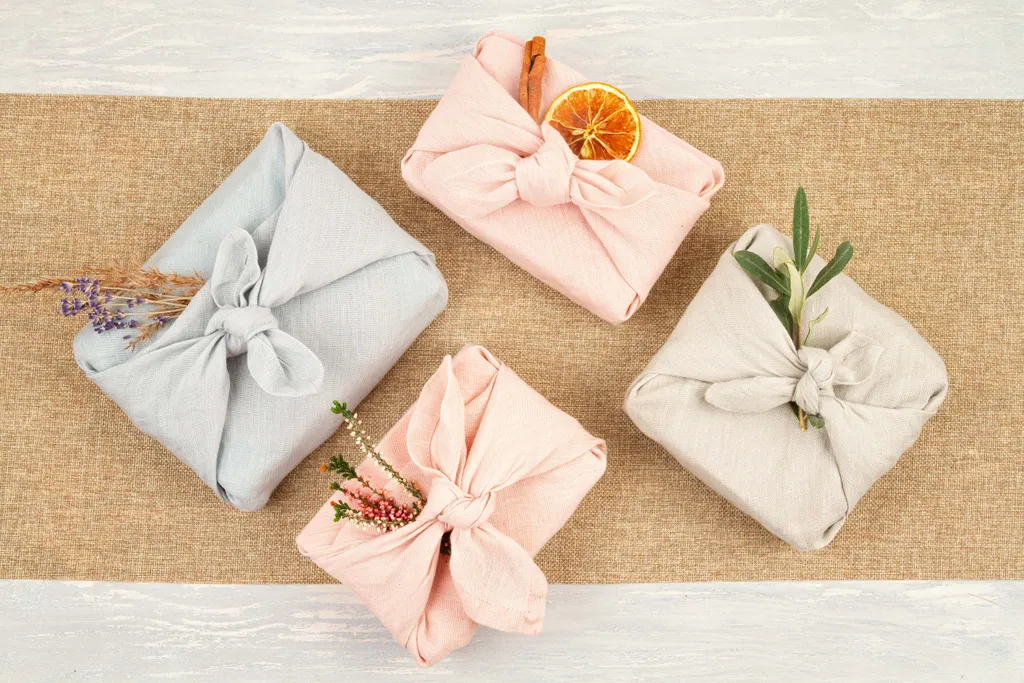 Vier in Stoff verpackte Geschenke, dekoriert mit Naturmaterialien, liegen auf einem Tisch mit Juteläufer