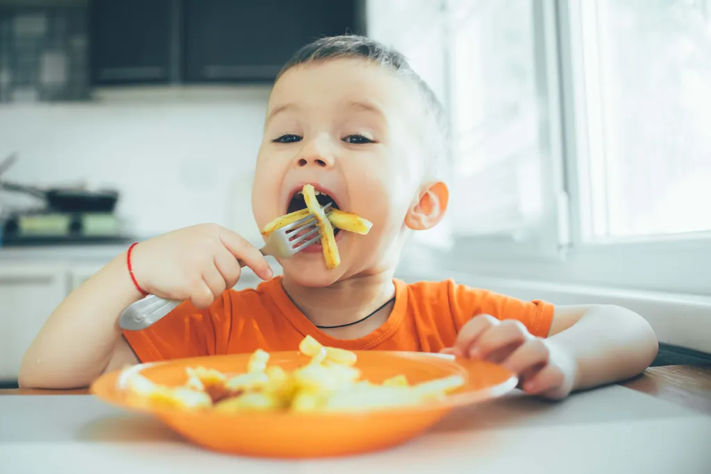 Fröhliches Kind isst knusprige Pommes, die in der Heißluftfritteuse zubereitet wurden