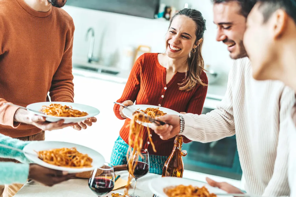 Freunde servieren frisch gekochte Pasta und genießen ein gemeinsames Essen in der Küche