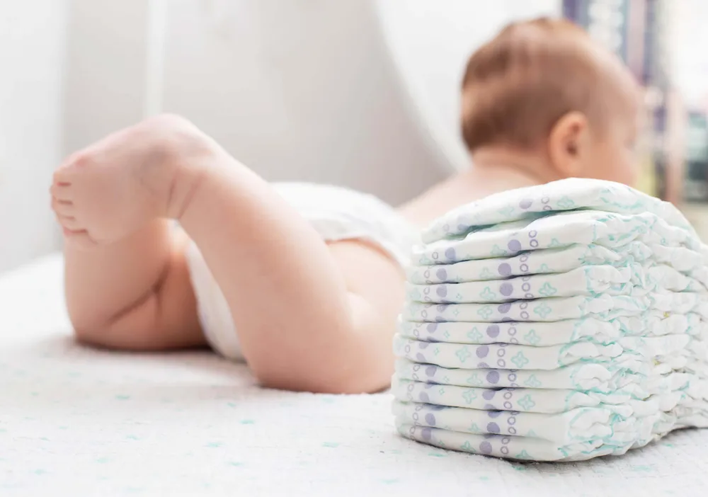 Baby liegt neben einem Stapel Babywindeln