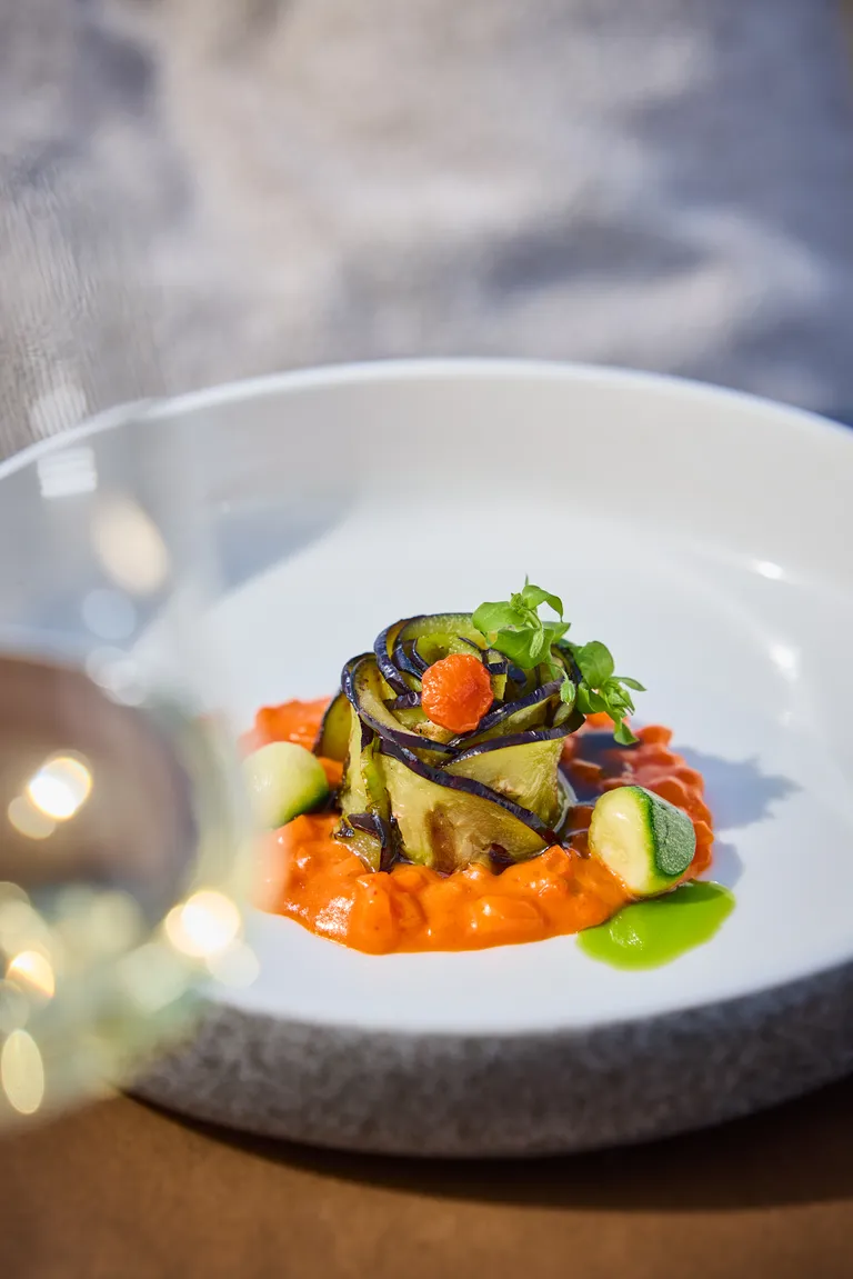 Fein angerichtetes Seewinkler Gemüse mit gerollter Melanzani, Zucchini, Paprika und Kräutern auf einem weißen Teller
