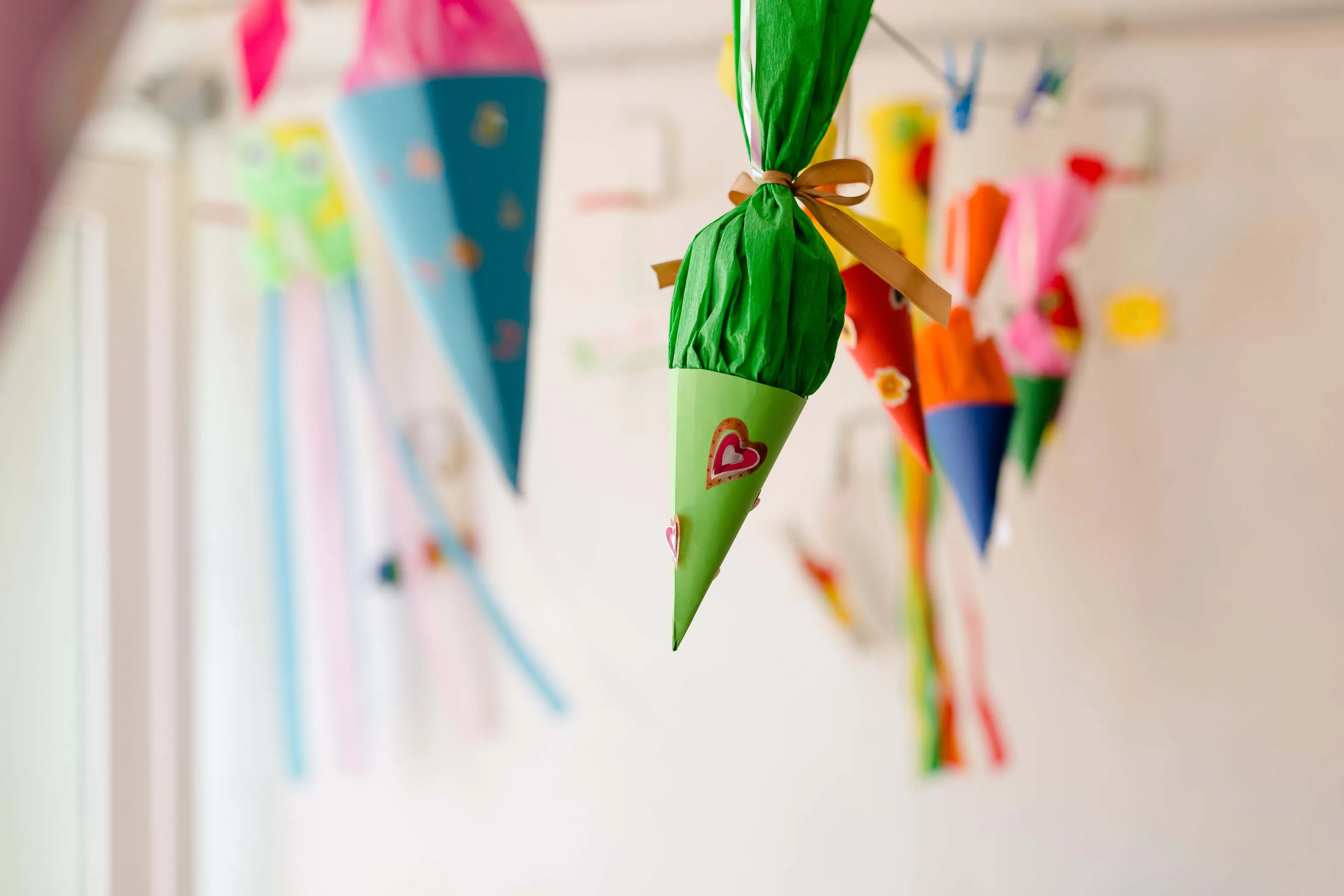 An der Decke hängen bunte Papierkegel, die mit Herzen und Schleifen verziert sind, wobei der Fokus auf einem grünen Kegel im Vordergrund liegt.