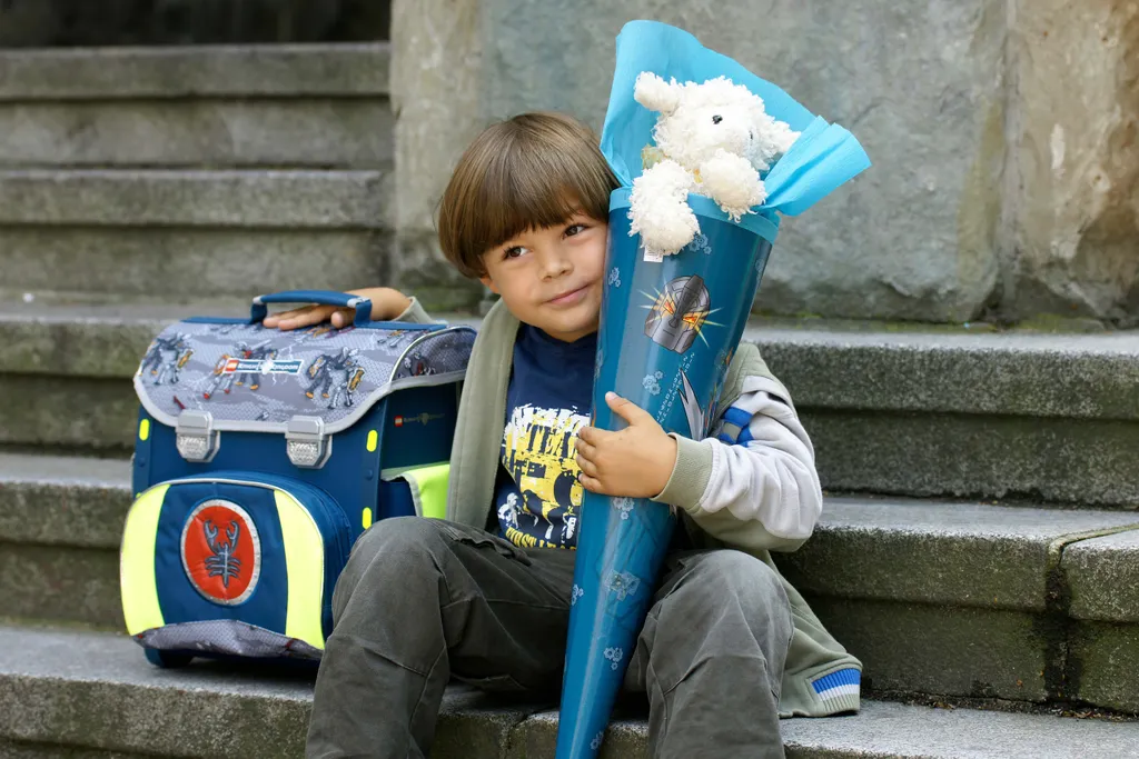 Schulkind sitzt mit Schultüte und Schulranzen auf einer Treppe