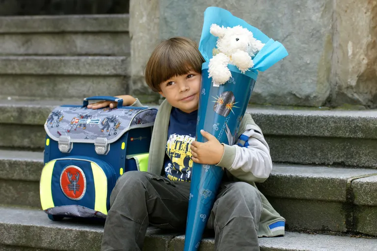 Schulkind sitzt mit Schultüte und Schulranzen auf einer Treppe