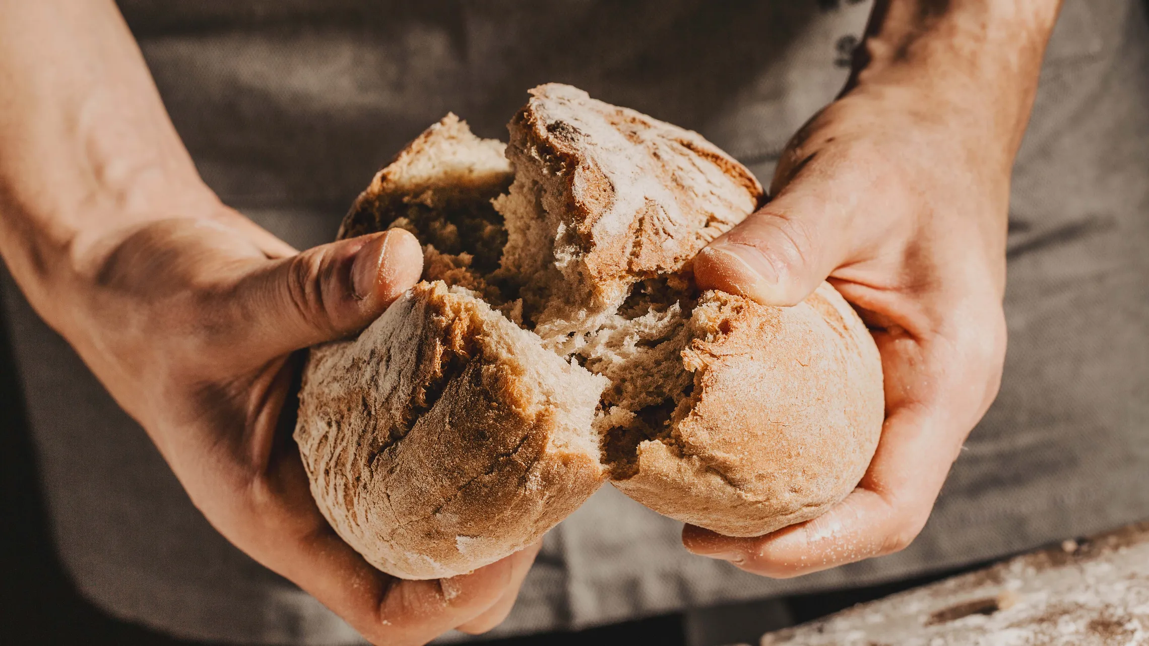 Eine Person beim Aufbrechen eines frisch gebackenen, grau-braunen Brotlaibes