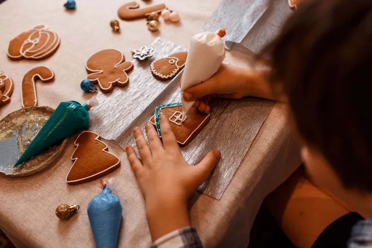 Eine Person verziert Lebkuchen in verschiedenen Formen mit weißem Zuckerguss aus einem Spritzbeutel.
