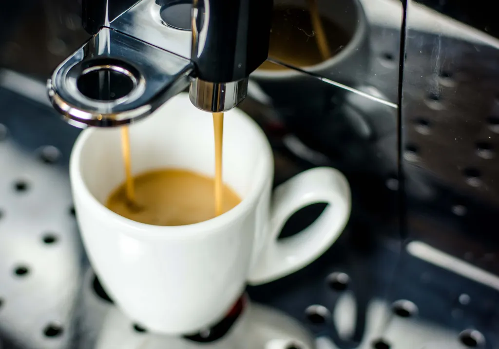 Frisch gebrühter Espresso läuft aus einer Kaffeemaschine in eine weiße Tasse