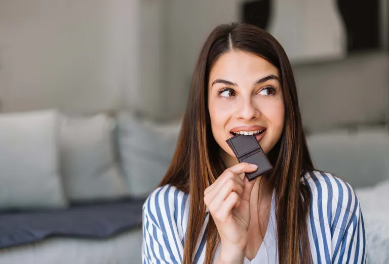 Junge Frau beißt in ein Stück dunkle Schokolade und genießt einen süßen Snack.
