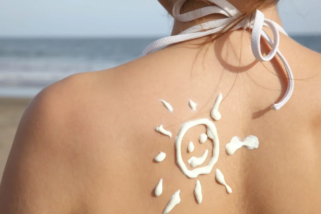 Eine Frau in einem Bikini an einem Strand die eine mit Sonnencreme gemalte lachende Sonne auf dem Schulterblatt hat