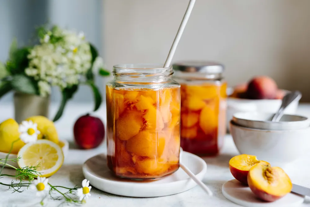 Eingekochte Pfirsiche im Glas mit frischen Pfirsichen und Zitrone