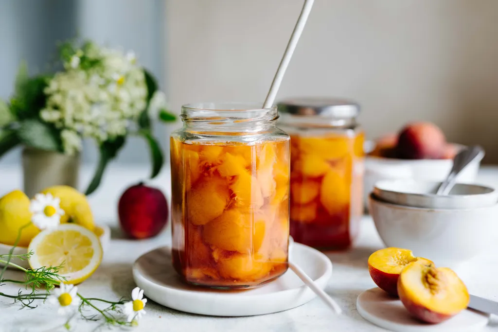 Eingekochte Pfirsiche im Glas mit frischen Pfirsichen und Zitrone