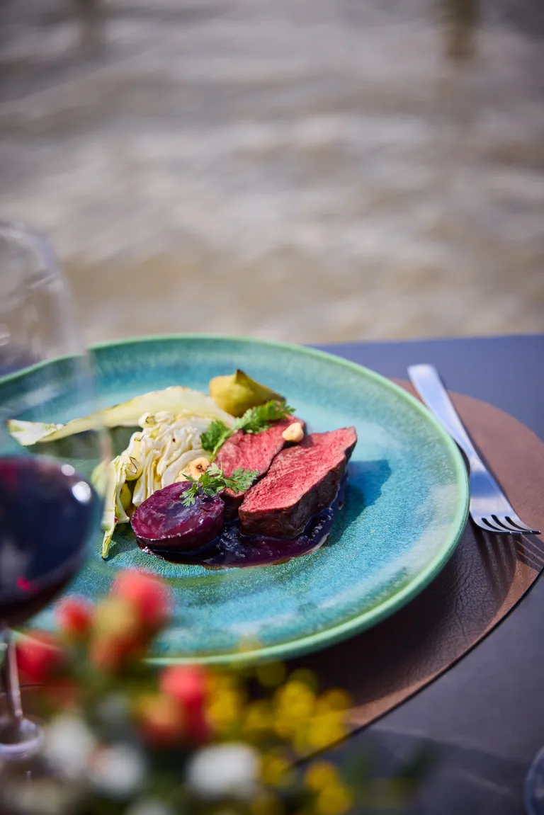 Rosa gebratener Fleischrücken mit geschmortem Kraut, violettem Gemüse, Kräutern und dunkler Sauce auf einem blauen Teller