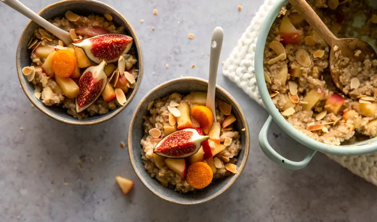 Cremiges Apfel-Zimt-Porridge mit Feigen, Äpfeln, Mandeln und Haferflocken in Schüsseln serviert