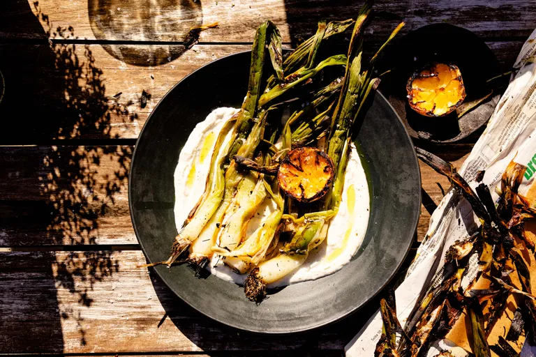Gegrillter Frühlingslauch mit Zitronenhälfte auf cremigem Dip, serviert auf rustikalem Holztisch
